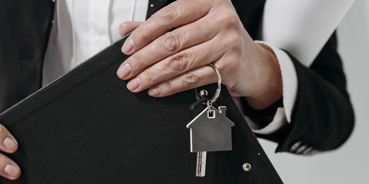 Une professionnelle de l'immobilier tient un porte-documents et un porte-clés en forme de maison, dans un appartement vide et lumineux.