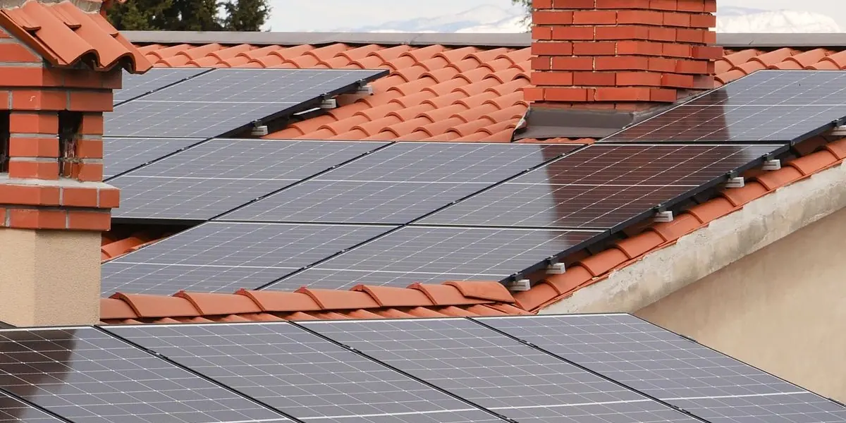 Des panneaux photovoltaïques posés sur les toitures en tuiles rondes de maisons méditerranéennes, entre cheminées de brique et cyprès.