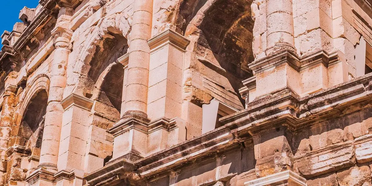 Les arènes de Nîmes, amphithéâtre romain à deux niveaux d'arcades, sous un ciel bleu.